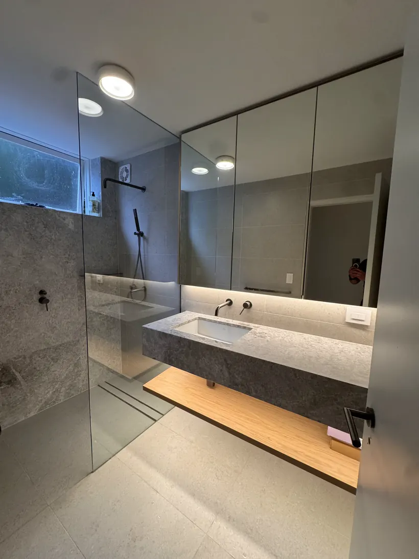 Concrete-look bathroom with a stone benchtop, floating oak shelf and lit mirror