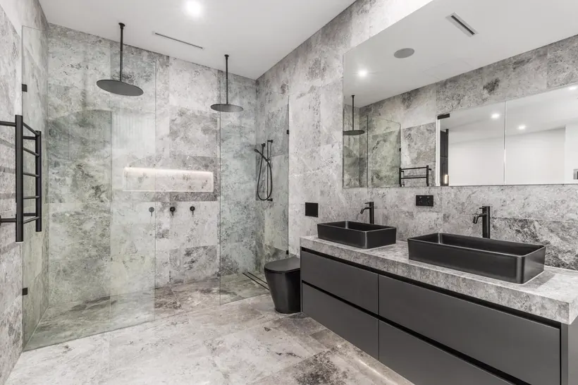 Double vanity in travertine with black basins, black tapware and a walk-in shower