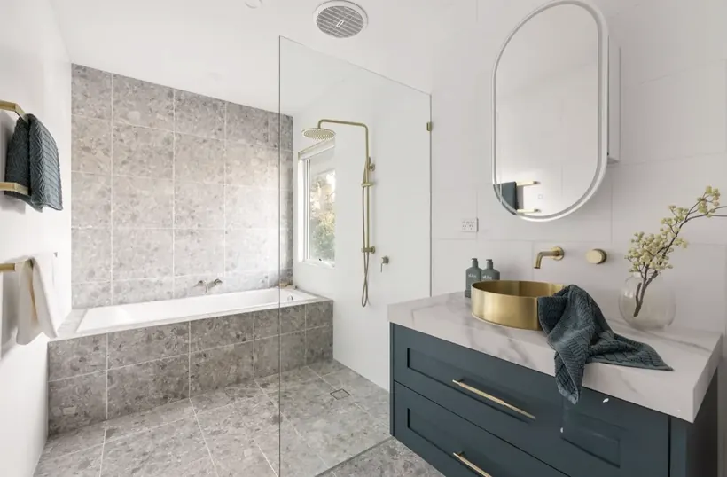 Teal vanity with brushed gold basins, a bath and a stone tiled feature wall