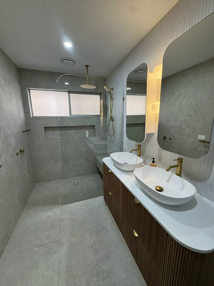 Double basins on a timber vanity below a backlit mirror in a warm stone bathroom
