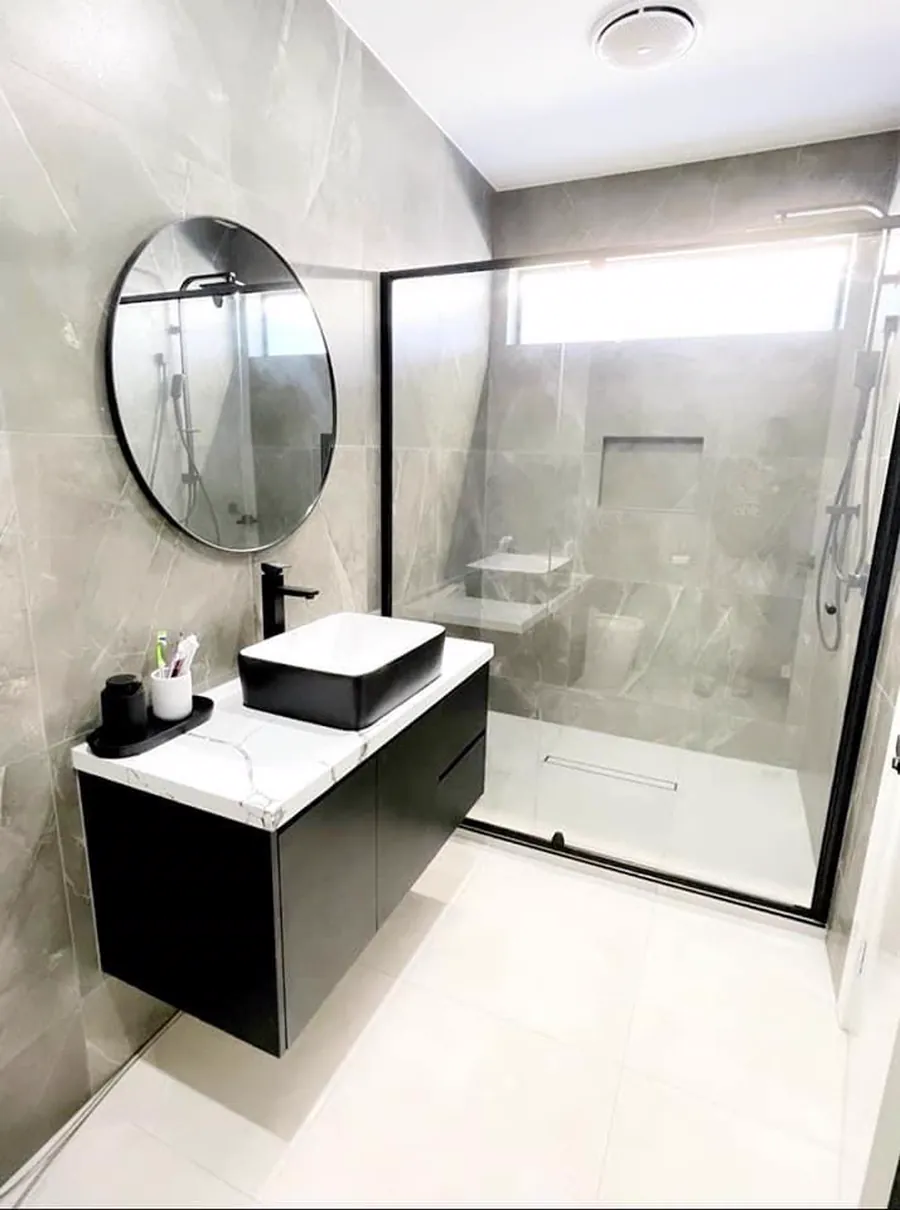 Compact ensuite with a round mirror, black vanity and a glass shower