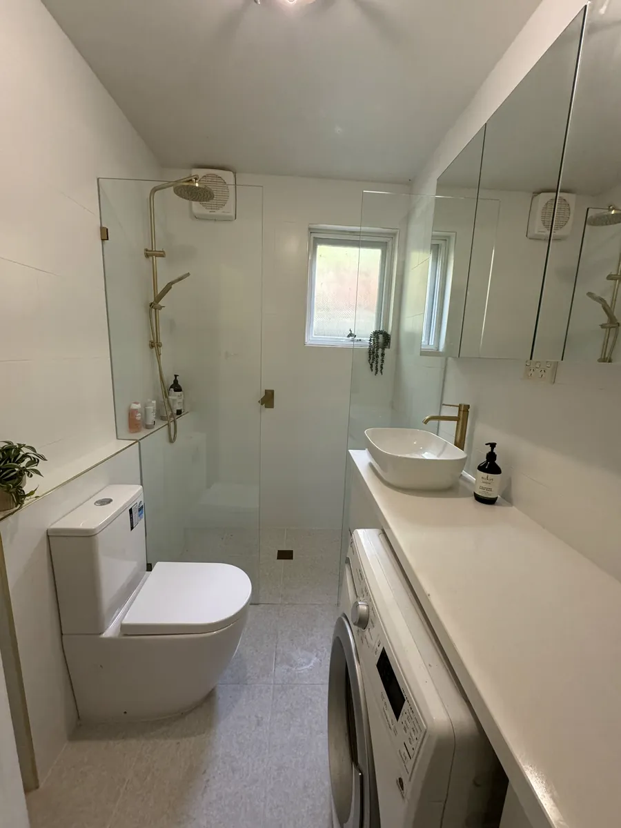 Combined bathroom and laundry with a washing machine set under a stone benchtop